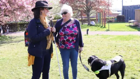 Two walking group members chatting and laughing. One of the members has a guide dog