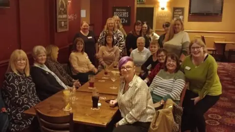 Supplied A group of 20 women sit around a long table in a pub. They are looking towards the camera and smiling. 