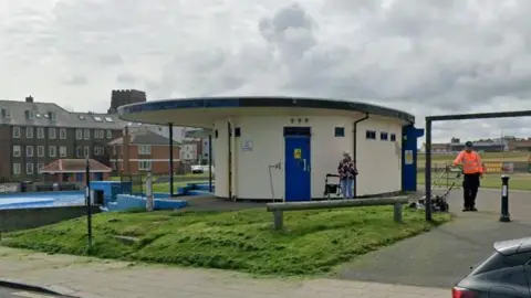 Google A public toilet on the West Cliff at Whitby - a small oval shaped building painted white with blue doors and small windows at roof level