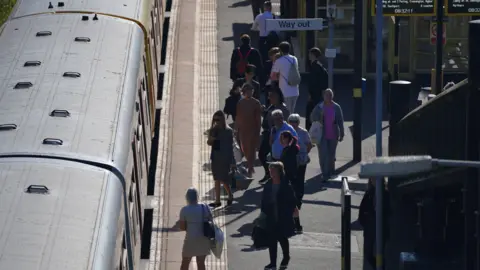 PA Media An elevated view of a group of passengers on the platform at Hunts Cross station approaching a train carriage which has just stopped. 