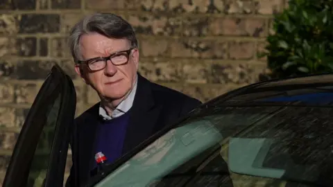 PA Media Lord Mandelson - wearing a dark jacket, light shirt and blue jumper - getting into a car