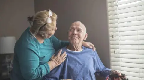 Getty Images A woman putting her arms around her husband in a wheelchair