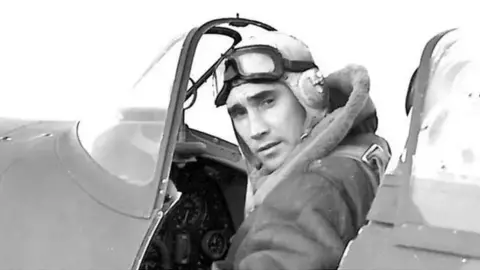 Battle of Britain Society A black and white image of test pilot Jeffrey Quill in the cockpit of a plane. He is wearing flying goggles over his head. He is looking over his left shoulder.