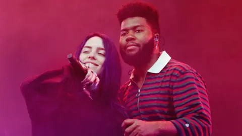 Billie Eilish and Khalid standing together on stage with red smoke