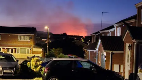 Claire Arthur View across a residential area towards glowing smoke on horizon against a twilight sky