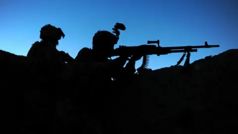 Two soldiers seen in silhouette against a blue sky
