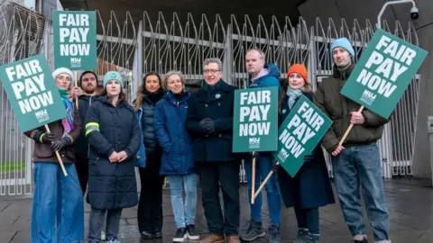 PA Media STV staff wearing coats holding big green NUJ signs outside the Scottish Parliament during previous strikes