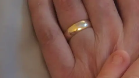 Jodie Smith A gold band is worn on the wedding finger of a man's hand which is shown in closeup.