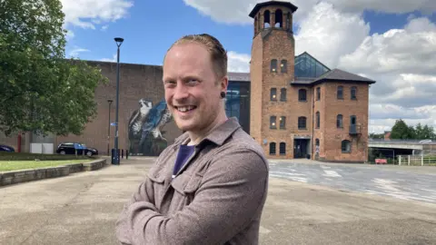 A man smiles in to the camera in front of the Derby Museum of Making.
