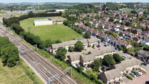 Ant Saddington/BBC An aerial view showing the existing four-track railway line just outside Bedford station. Two short streets of modern terraces are immediately to the tracks' right, with dozens of older Victorian houses in the streets beyond. There is a green space above Julia Virdee's road. 