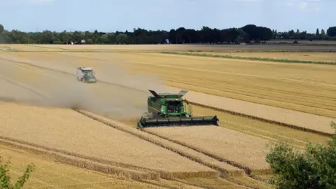 PA A combine harvester is harvesting a field of wheat with another tractor behind 