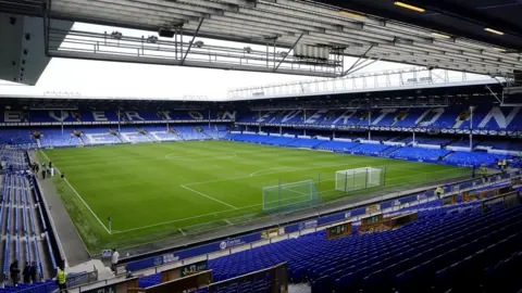 PA Media Inside Goodison Park is the football pitch surrounded by a sea of blue seats. In white writing along the seats it reads "Everton" and "EFC".