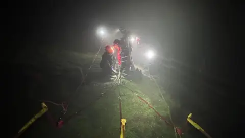 A crag rescue system's straps being set up at night in foggy conditions