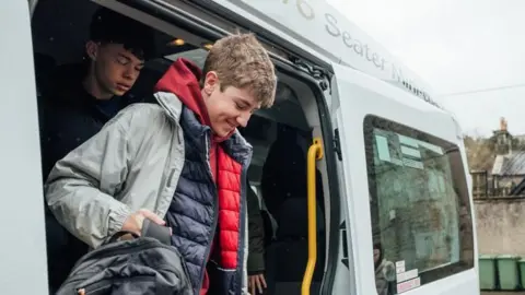 Two teenage boys get out of a minibus