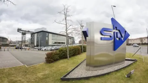 An STV sign outside the HQ building in Glasgow with the Finnieston Crane and the Hydro in the background
