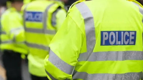 Stock image of the back of a police officer wearing a fluorescent jacket.