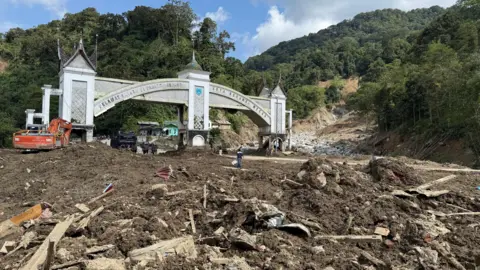BBC / Silvano Hajid A large amount of mud and debris lies in front of an white and grey stone arch on a mountain pass in Indonesia