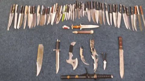 A large number of knives collected by police. The image is slightly blurred, showing a number of knives left on a blue floor. 