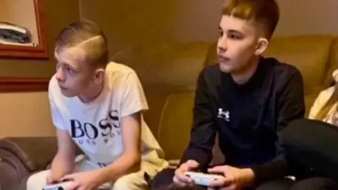 PA Media Mason Rist and Max Dixon. Both boys are sat playing games consoles. They are not looking at the camera.