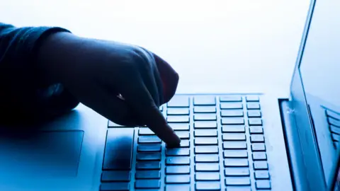 A child's hand pressing a key of a laptop keyboard.