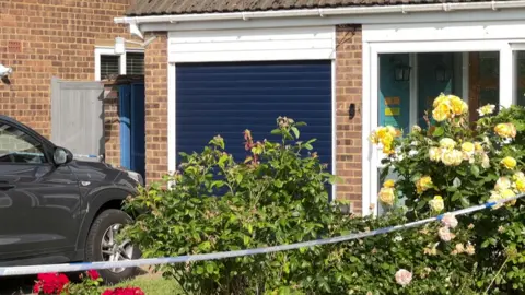 The front of a residential house with blue garage with flowers planted in a border aside it. 