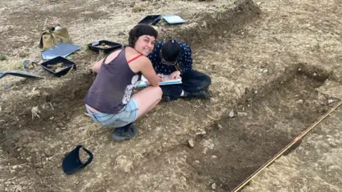 RAU A photo showing Dr Cassie Newland from The Royal Agricultural University crouched down at the site of an archaeological dig