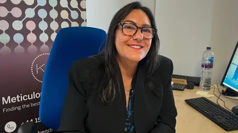 woman in suit jacket sat at desk in office 
