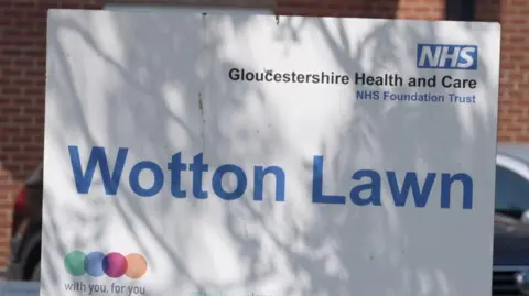 A sign outside a brick building at the Wotton Lawn hospital. There's an arrow pointing in the direction of the Maxwell Centre. 