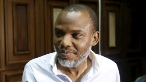 Reuters A head-and-shoulders shot of Nnamdi Kanu, in an open-necked white shirt, looking to the left of the picture. He is in a wood-panelled court room. 