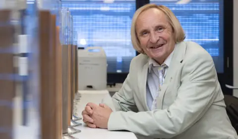 Fiona Wolf - University of Sydney Alex McBratney has blond hair and is wearing a greyish suit jacket with a patterned tie and plain shirt underneath. He looks like he is possibly in a laboratory