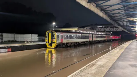 Bic Bickerton A train at a train station with the tracks completely submerged by brown flood water