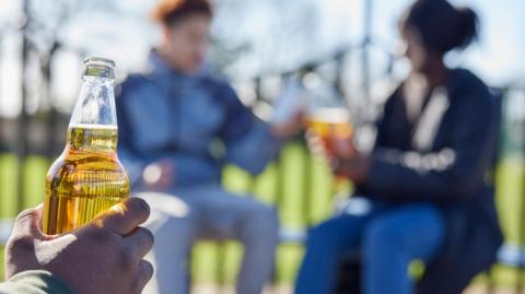 Teenagers drinking in a play area with an open bottle of cider 