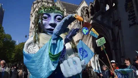 Getty Images A large blue puppet holding an empty plastic bottle is carried by campaigners outside the Royal Courts of Justice in London
