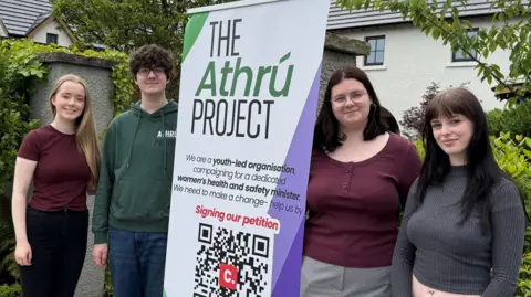 Four young people standing around a poster which says 'The Athrú Project'