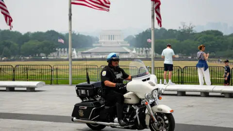 A US Park Police officer sits on a motorbike in front of the Washington Monument, with American flags in the background