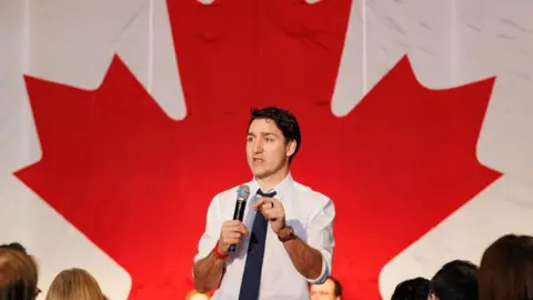 Justin Trudeau speaking in front of a giant Canadian flag at Friday's summit