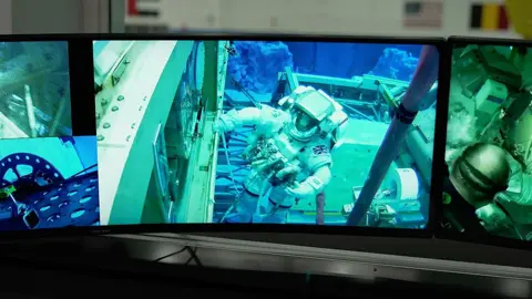 Kevin Church/BBC Astronaut Rosemary Coogan is seen on a TV monitor, training underwater in her spacesuit at the Johnson Space Centre, Houston, Texas. She is holing onto a handrail on the outside of the mock up of the space station with her right hand. The Union Jack on her left shoulder is clearly visible. 