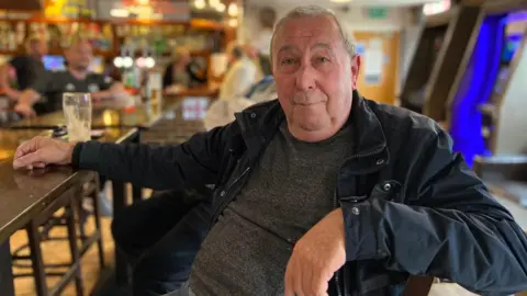 BBC/Emily Coady-Stemp Stuart Noakes sits at a table in a social club