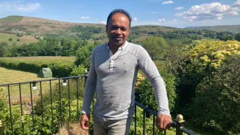 Neelanga Uggalle standing in his garden with a view of the surrounding countryside.