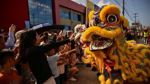 Getty Images A Chinese New Year dragon costume dances in a crowd on a street in Panama in front of a building that says "El Dorado"