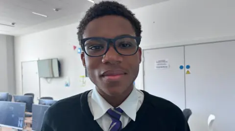 Kate Bradbrook/BBC A boy in a school uniform wearing dark-framed glasses.