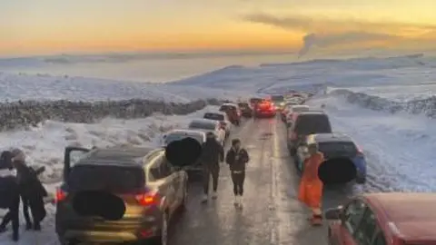 Rows of cars on both sides of a road high up in a snowy Peak District