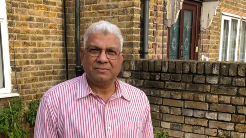 Mohammed Bahar standing in his garden wearing a pink striped shirt looking direct at h 