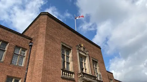 Dudley Council The flag of the Black Country is flying at the top of a large brick building. The flag is black, white and red with chain representing the region's manufacturing heritage.