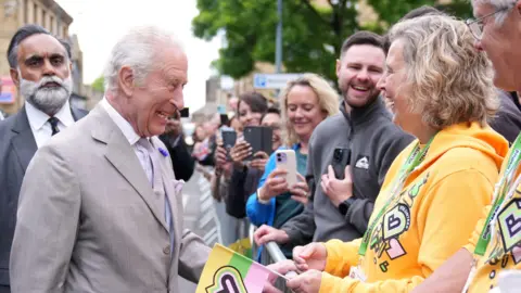 King Charles meeting a woman in a queue wearing Bradford City of Culture hoodie and holding City of Culture flag