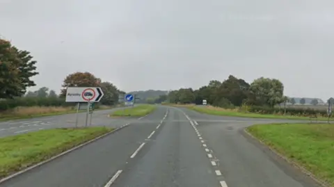 Google A dual carriageway junction. Grass verges can be seen on either side. The sky is grey.