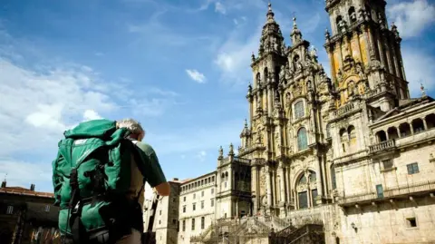 Reda The back of a man wearing a rucksack in the foreground looks ahead to a church