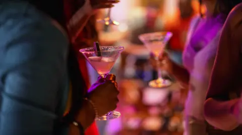 Getty Images Close-up of a martini glass held by a female at a bar with purple lighting