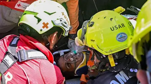 Federico PARRA / AFP vía Getty Images Un equipo internacional de rescate asiste a Hernán Gil, sobreviviente de los dos terremotos de Venezuela, en Catia La Mar, estado de La Guaira, Venezuela, el 2 de julio de 2026, ocho días después del sismo. Hernán Gil, un guardia de seguridad de 43 años, quedó sepultado en la cabina del edificio de siete pisos donde trabajaba en Catia La Mar, una zona costera del estado de La Guaira devastada por el desastre.
