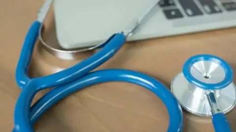 A blue stethoscope next to a laptop computer on a wooden table.